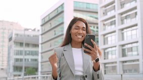 African American joyful trader business woman with cellphone app, rejoices in the news reads from the smart phone stock good news. Black lady get money, reward standing at outdoor office. Winner bet - Powered by Shutterstock - Get 15% off with code: PIKWIZARD15