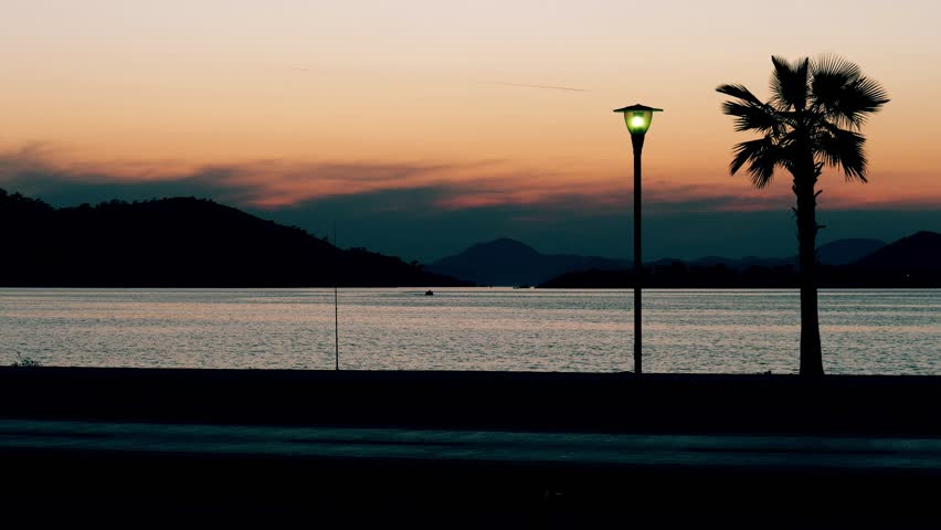 Silhouettes of walking people and riding cyclist on the seaside at sunset. Fethiye, Turkey