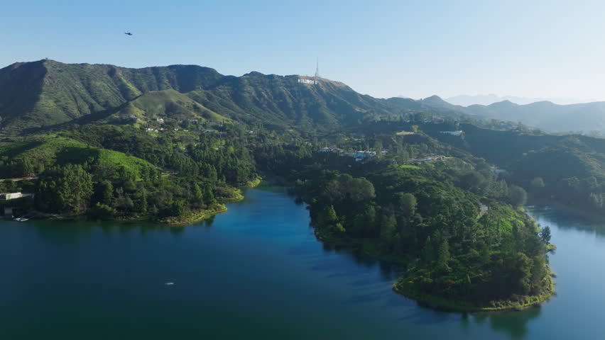 Scenic aerial above blue Hollywood lake reservoir with deep blue water on green Hollywood hills, Los Angeles California USA. Scenic aerial shot expensive houses in green forest on sunny summer day 4K