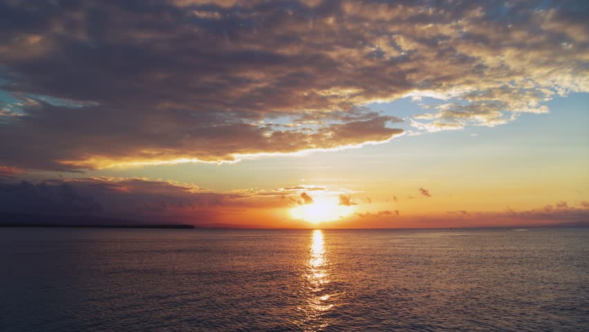 Bright background of sea sunset, view from the beach. A yellow sun in a blue sky with orange clouds over the Caribbean Sea. Beautiful evening seascape. Sun glare on the water. Twilight.
