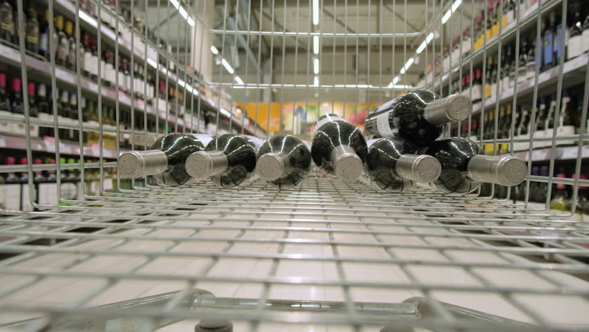 View from shopping cart with bottles of wine to rows of shelves with assortment of alcoholic products. 