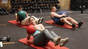 Sporty young girl doing twisting sit-ups with medicine ball to strengthen abs muscles during group training in gym. Active lifestyle concept . High quality 4k footage - Powered by Shutterstock - Get 15% off with code: PIKWIZARD15