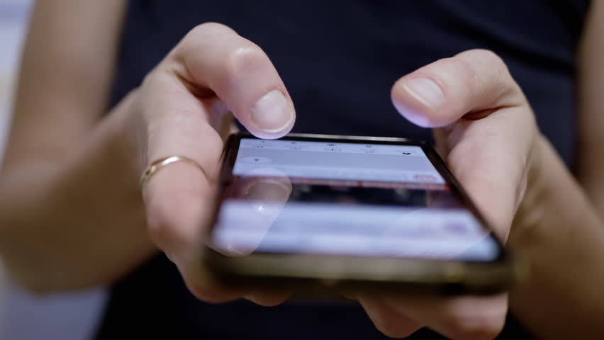 Female Fingers Scroll through the News Feed in Social Networks on a Mobile Phone. Close-up. A woman browsing mobile applications on a smartphone. Fingers touch the screen. Life in a smartphone.
