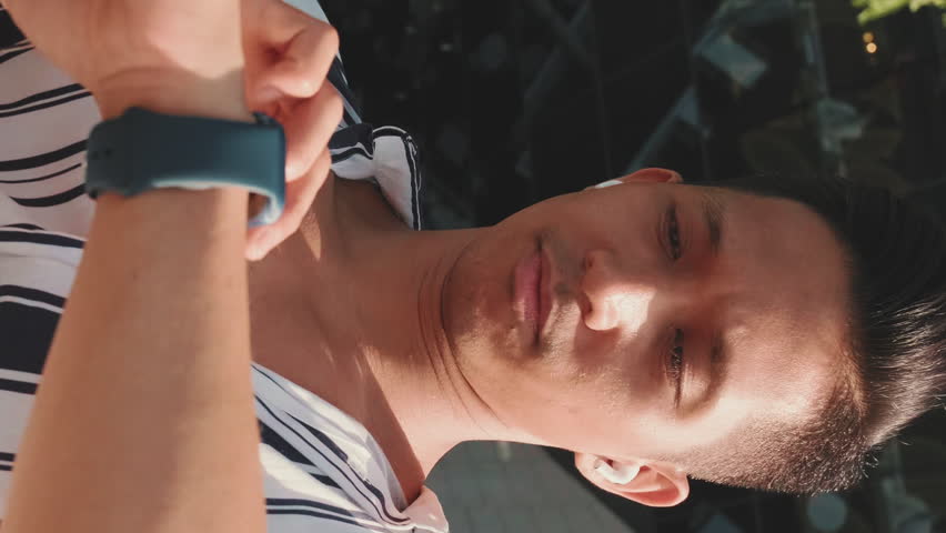 VERTICAL VIDEO: Close-up of young man looking at smart watch