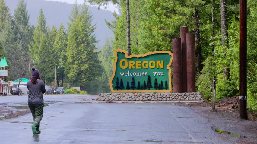 Woman, 30s, walks up and takes photo of Oregon welcomes you sign on Redwood Highway.