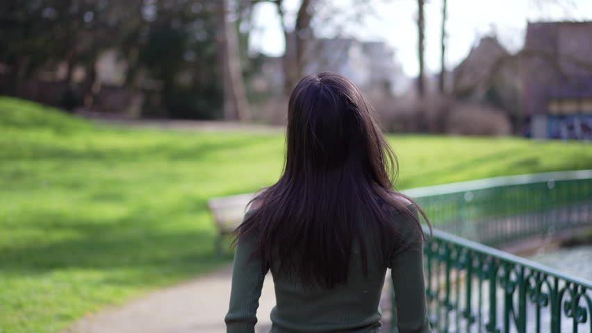 One joyful young woman turning head toward camera while walking outside at park. Tracking shot of a happy adult girl spinning while smiling Royalty-Free Stock Footage #1102412805