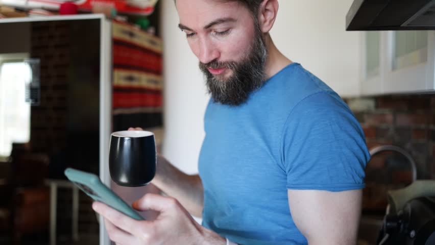 Handsome man enjoying time for internet and coffee in kitchen at home.