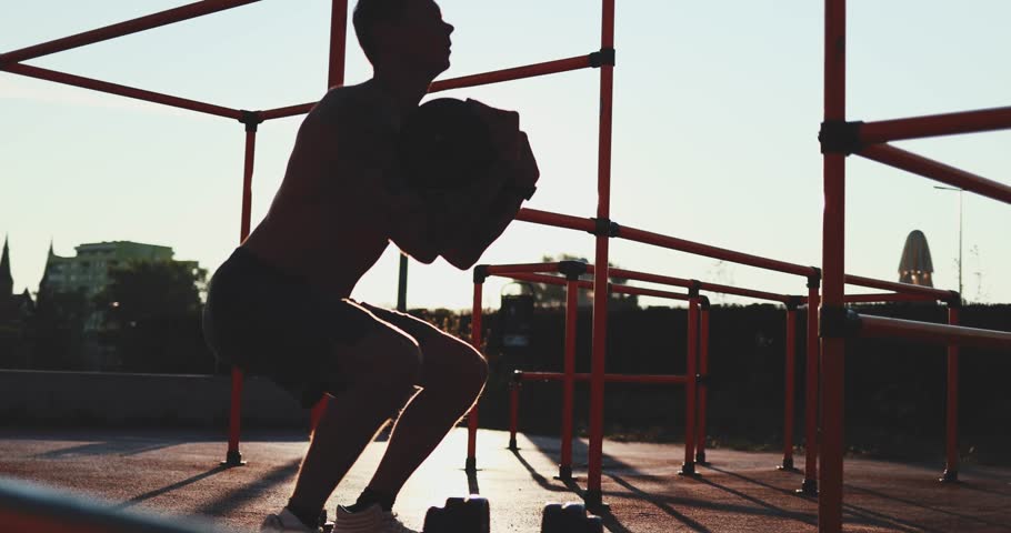 Sports Man works out at sunrise at outdoor fit park gym. Athlete lifts weights at sunset, functional training with equipment, building muscles and strength for heath and fit look.       Royalty-Free Stock Footage #1102421373