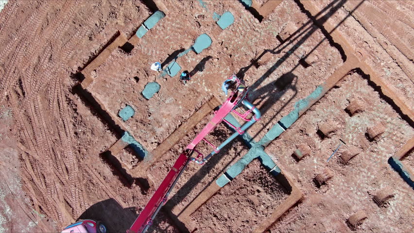 Worker pours concrete for foundation of building while controlling automatic pump to pour cement concrete