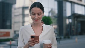 Beautiful Business Woman Using Smartphone While Walking Near Her Workplace on the Coffee Break. Female Looking at the Smartphone Screen Holding Drink. Girl Stylish Appearance - Powered by Shutterstock - Get 15% off with code: PIKWIZARD15