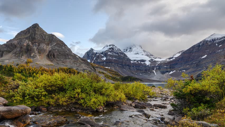 Time lapse scenery of Mount Assiniboine with stream flowing to Lake Magog in autumn forest on sunny day at Assiniboine provincial park, BC, Canada