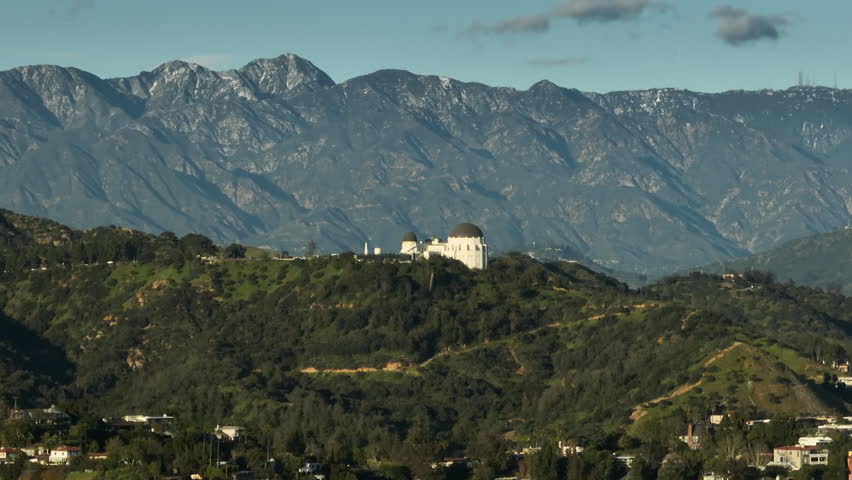 Epic aerial helicopter view of Los Angeles USA. California landmark famous Griffith observatory and park on green hills with high mountain peaks under blue sky on motion background Royalty-Free Stock Footage #1102424773