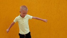 A little cheerful boy jumps and has fun against the background of a yellow wall in the courtyard of the house.