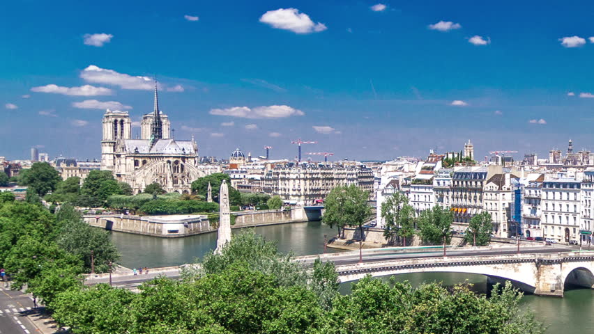 Paris Panorama with Cite Island and Cathedral Notre Dame de Paris on a background timelapse from the Arab World Institute observation deck. Top view. Green trees, Seine river, Blue cloudy sky. France