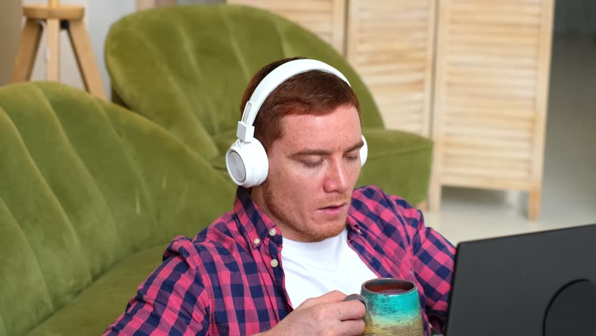 Coffee breaks help revitalize tired workers and maintain productivity, red-haired, freckled man drinking coffee while working on his laptop. significance of taking breaks to sustain productivity. Royalty-Free Stock Footage #1102433339