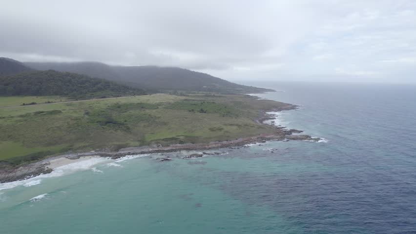 Aerial View Of Beaumaris Beach, Green Hills And Mountains On Overcast Day - Tasman Sea, Tasmania, Australia.