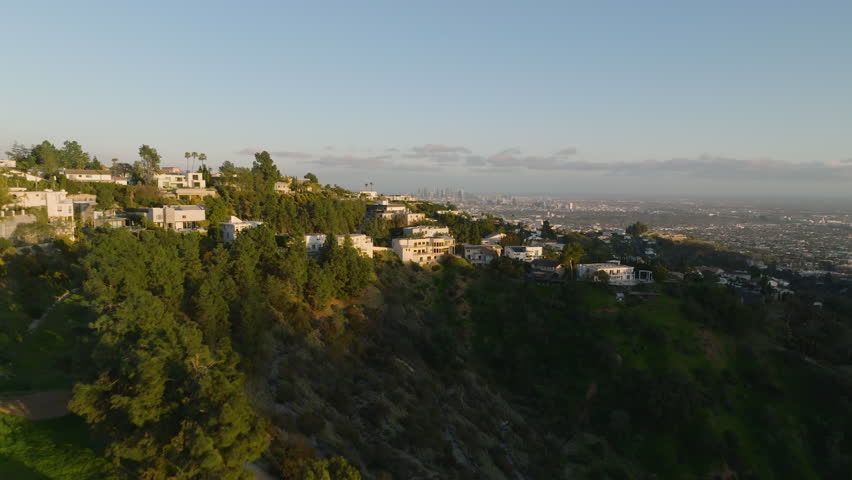 Backwards reveal of luxury residences in hills above metropolis. Hollywood Hills at golden hour. Los Angeles, California, USA
