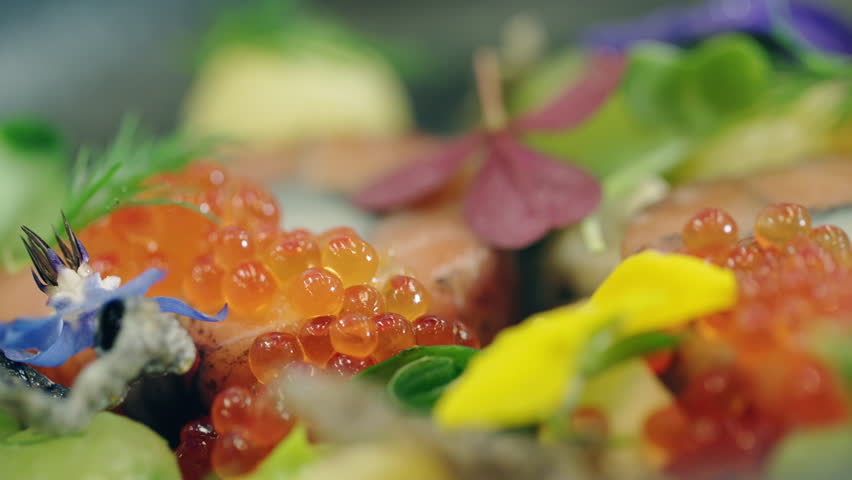 Macro close-up shot of master chef carefully placing a blue flower on red fish roe gourmet dish with tweezers. Fine dining and food decoration. Royalty-Free Stock Footage #1102442545