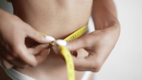 A girl is measuring her waist with a centimeter tape. The woman is taking waist scale tape and showing her. Concept of losing weight ideal figure slim stomach and proper nutrition. Close up. - Powered by Shutterstock - Get 15% off with code: PIKWIZARD15