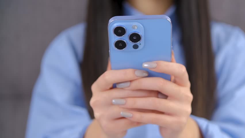 Girl typing a message on cellphone. Unrecognizable female texting online with a modern blue smartphone. Person writing a comment on a social media app Royalty-Free Stock Footage #1102448115
