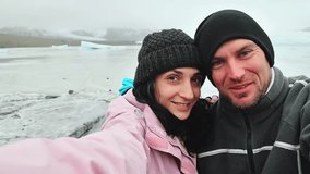 Happy adventurous couple taking selfie in front of glacier lagoon in Iceland. Two tourists having fun on romantic winter vacation in Iceland - Holidays and traveling lifestyle concept