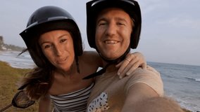 
Young couple taking selfie on scooter at sunset by the beach. Two people exploring Sri Lanka with motorbike taking video selfie chatting online with friends sharing adventures 