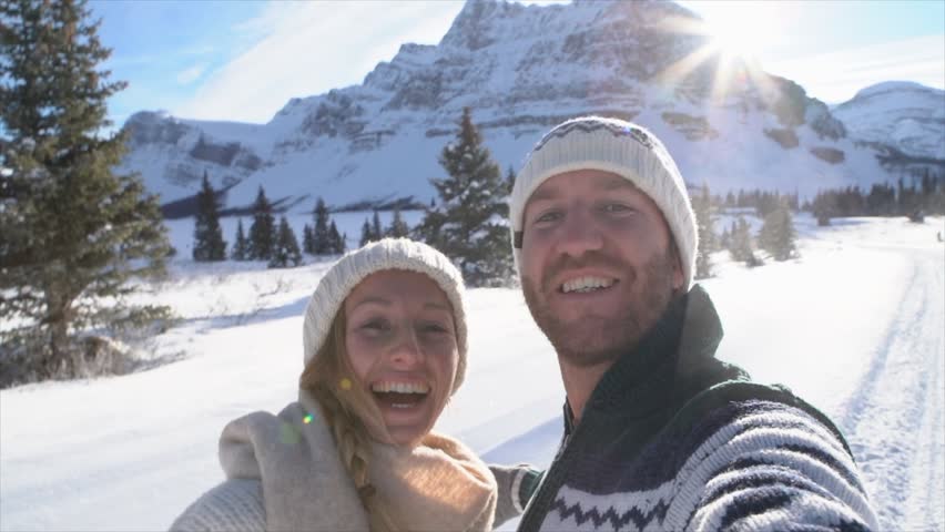 SLOW MOTION: Young couple taking selfie on frozen mountain lake having fun in winter vacations. Couple having video chat outdoors in winter snowy landscape