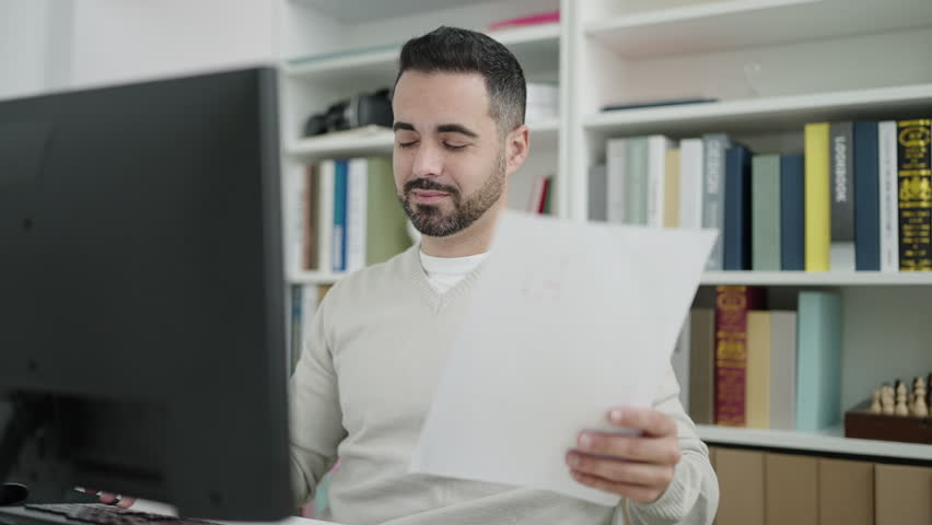 Young hispanic man student using computer reading document at library university