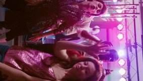 Vertical video: POV of happy adults enjoying disco party at club, having fun together on modern electronic music. Friends dancing and partying in discotheque, jumping under stage lights. Handheld shot