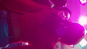 Vertical video: Men and women dancing at nightclub and listening to music, having fun at club with stage lights. Group of persons enjoying social gathering with friends on dance floor. Handheld shot.