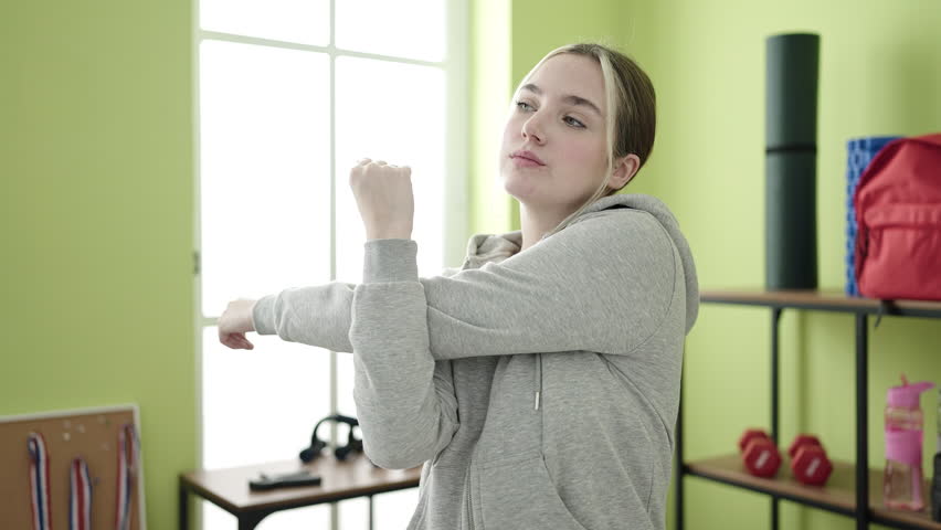 Young blonde woman stretching arms at sport center