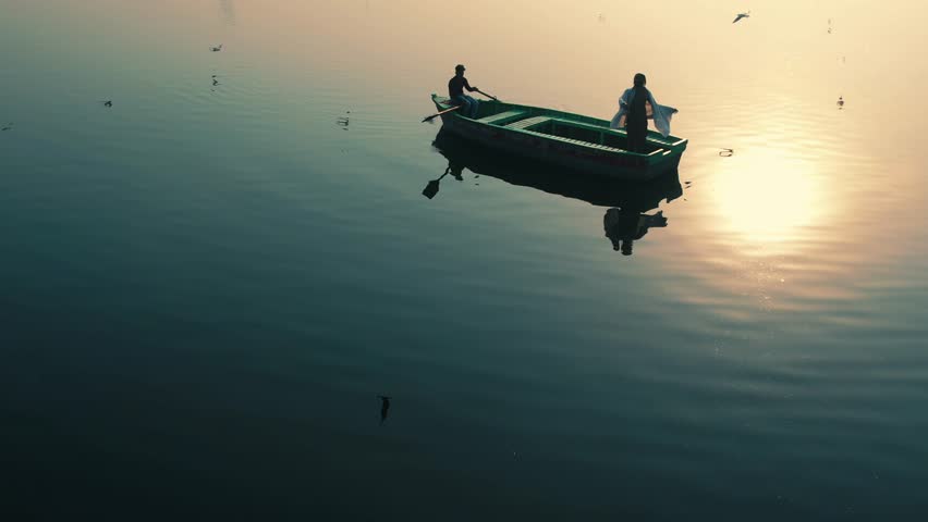 Aerial view of a boat sailing along the Yamuna river at sunset surrounded by seagulls along the coast in New Delhi, India. Royalty-Free Stock Footage #1102459141