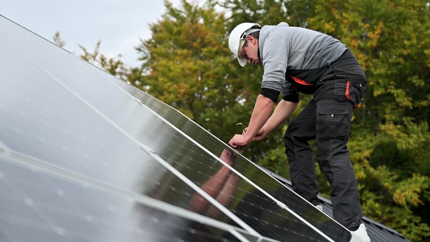 Man technician mounting photovoltaic solar panels on roof of house. Engineer in helmet installing solar module system with help of hex key. Concept of alternative, renewable energy. Royalty-Free Stock Footage #1102460425