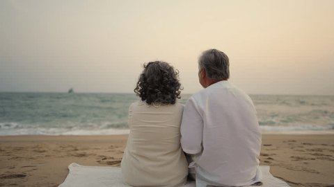 4K Happy Asian family senior couple with gray hair resting together at tropical beach at summer sunset. Retired elderly people enjoy romantic outdoor lifestyle travel nature ocean on holiday vacation. Adlı Stok Video