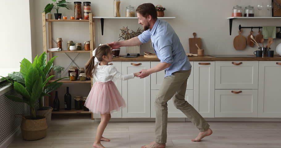Happy young dad teaching pretty little daughter in ballet skirt to dance, holding kids hands, having fun, enjoying activity at home. Cute girl in pink princess dress training choreography with daddy Royalty-Free Stock Footage #1102463611