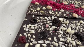 Dark chocolate bars with nuts and berries rotating on the plate video. High quality 4k footage