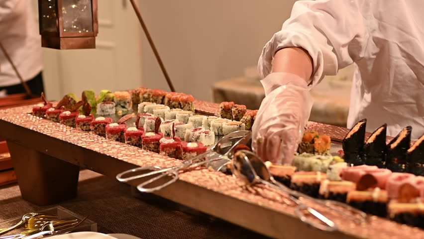 Male chef's gloved hands placing sushi on mirror table. Traditional Japanese cuisine. Close-up of chef serving delicious sushi in interior. Royalty-Free Stock Footage #1102467419