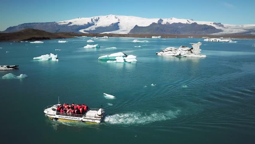 Aerial drone footage of an amphibian boat sailing among icebergs in Jokulsarlon glacier lagoon, Iceland. Scenic view of an Artic nature ice landscape. Melting glacier. Global warming, climate change.
