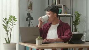 Asian man drinking coffee and looking to computer he is smiling  after work finish