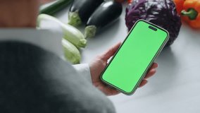 Modern Smartphone With Green Screen For Chroma Key Montage In Hand Of Mature Woman in Kitchen