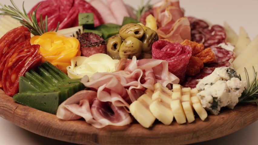 Charcuterie and cheese platter rotates smoothly around its axis. Appetizers boards with assorted cheese, salami, ham, grape and nuts. Top view. Video is looped