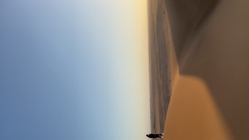 Vertical video. A young woman walks along sandy dunes in Namibia. Summer vacations, wild desert nature in Africa. Dune 45 or 17 at sunset or sunrise.