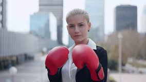Aggressive stylish businesswoman looking at camera wearing boxing gloves outdoors - Powered by Shutterstock - Get 15% off with code: PIKWIZARD15