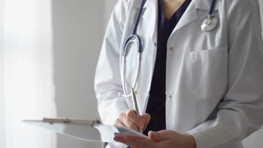 Doctor woman at work using a white clipboard while writing medical notes. An unknown physician standing near the panorama window in hospital. Medicine Royalty-Free Stock Footage #1102484529