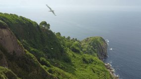 Pan up onto cliffs just outside of San Sebastian, Spain with birds flying around ancient ruins
