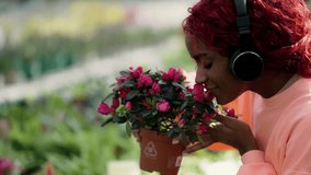 A young woman in headphones thoughtfully inhales the scent of pink plants in the greenhouse - Powered by Shutterstock - Get 15% off with code: PIKWIZARD15