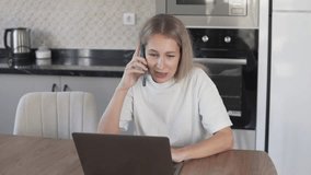 A beautiful woman is talking on the phone at home at the computer and talking to a client.
