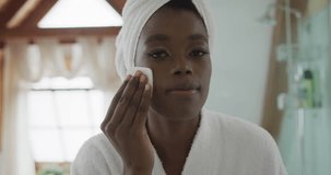 Animation of icons over african american woman cleansing face in bathroom. Global lifestyle, self care and digital interface concept digitally generated video.