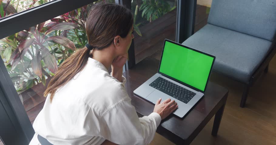 Laptop with green screen. Female hands typing and scrolling on a track pad. Back view of woman sitting at wooden table and looking at computer with green screen in coffee shop Royalty-Free Stock Footage #1102498449
