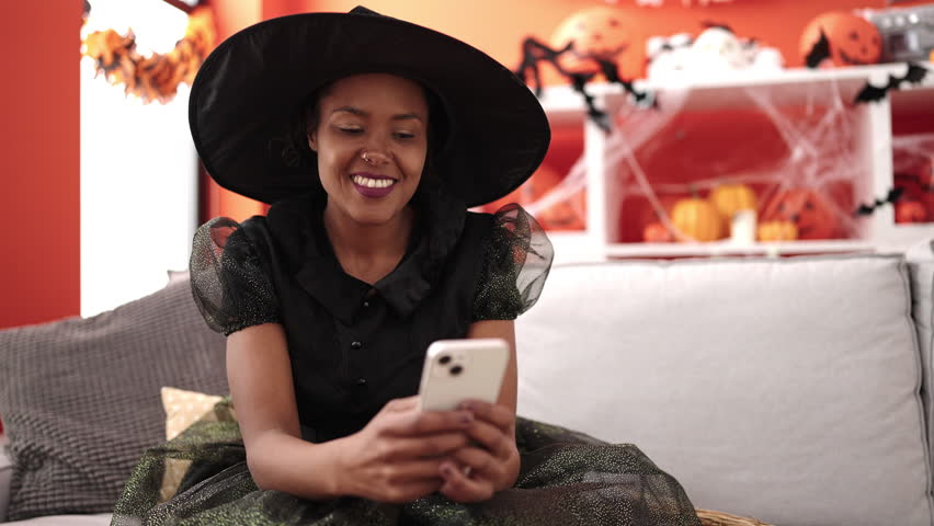 African american woman wearing witch costume using smartphone at home
